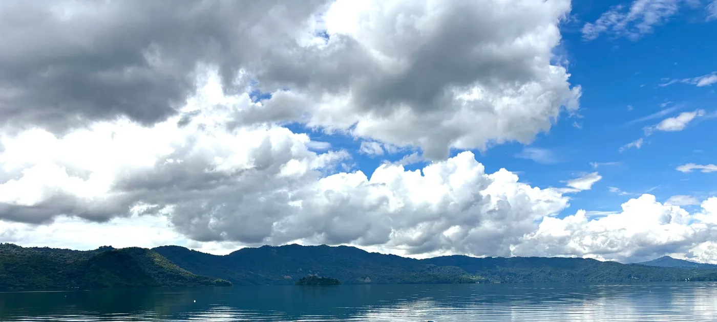 Calm water of Lake Coatepeque under large white clouds